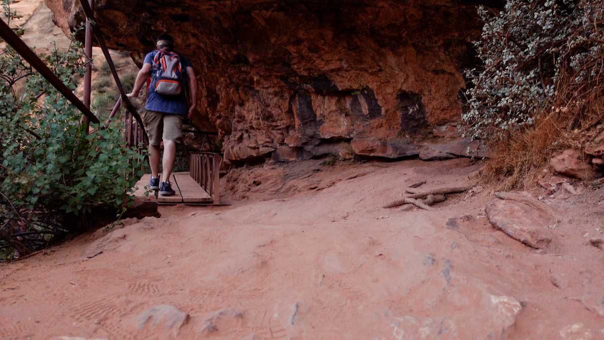 A hiker walks on a wooden catwalk at the edge of canyon