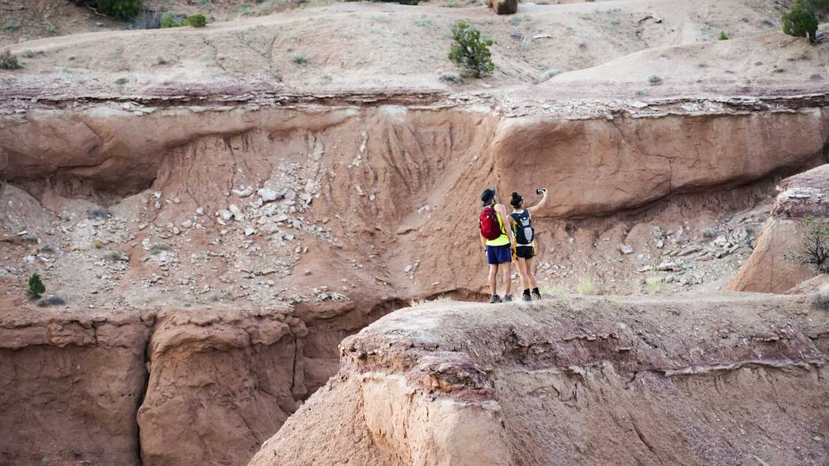 Two hikers take self portrait on top of narrow overlook of red rocks