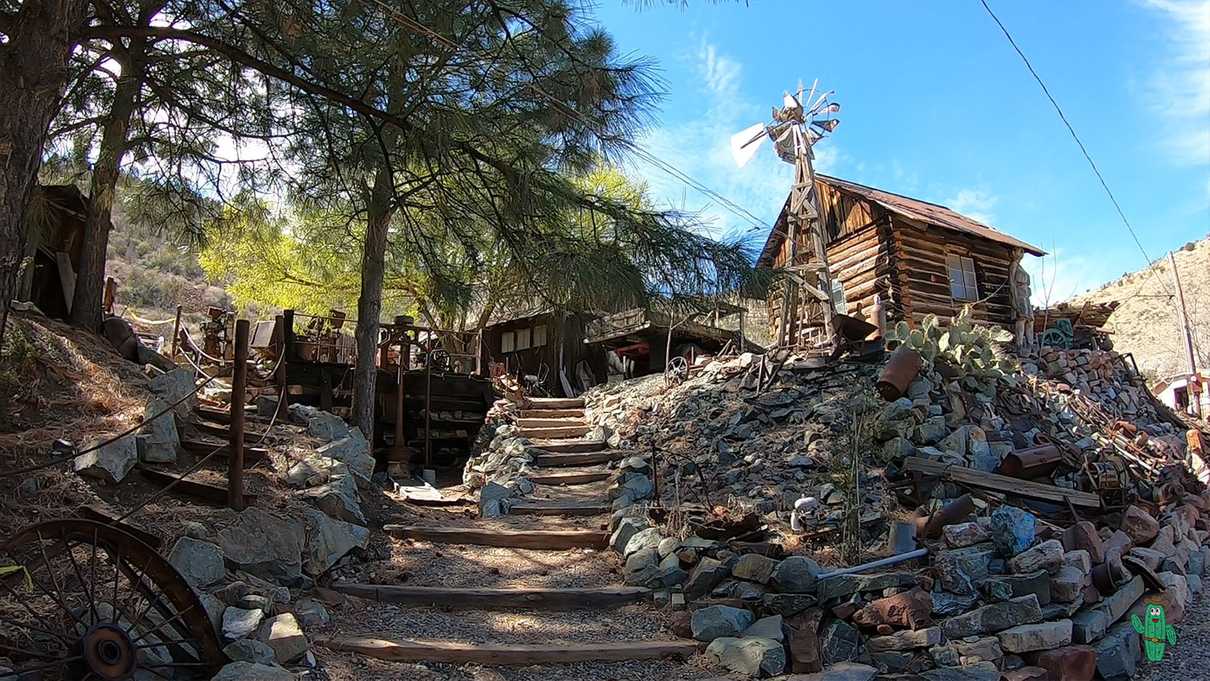 Small cabin and windmill atop a hillside littered with rusted mining equipment