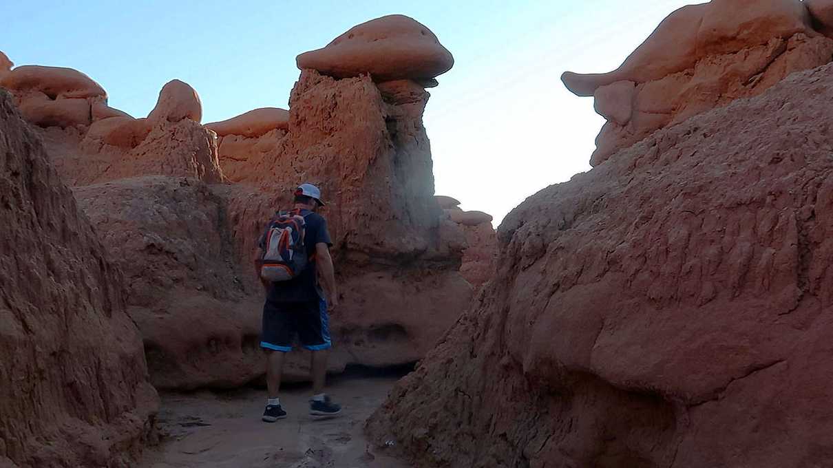 Male hiker walking through canyon of red stone features