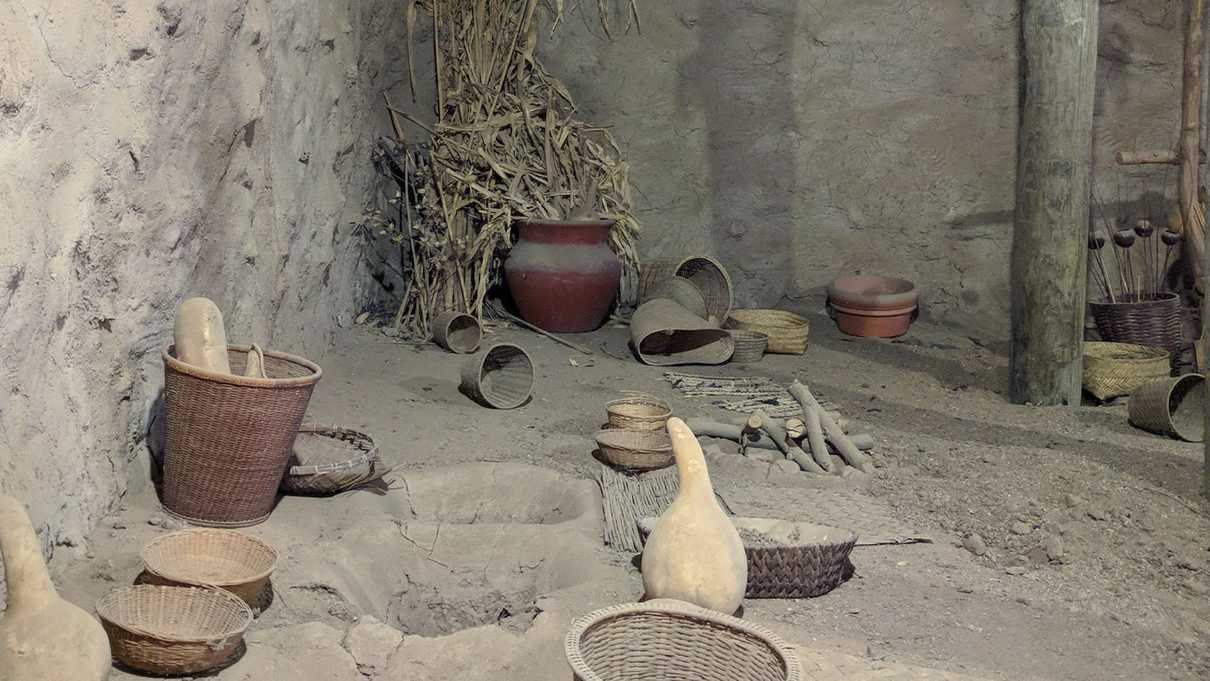 Scattered squash, woven baskets and pottery in a dirt floored room