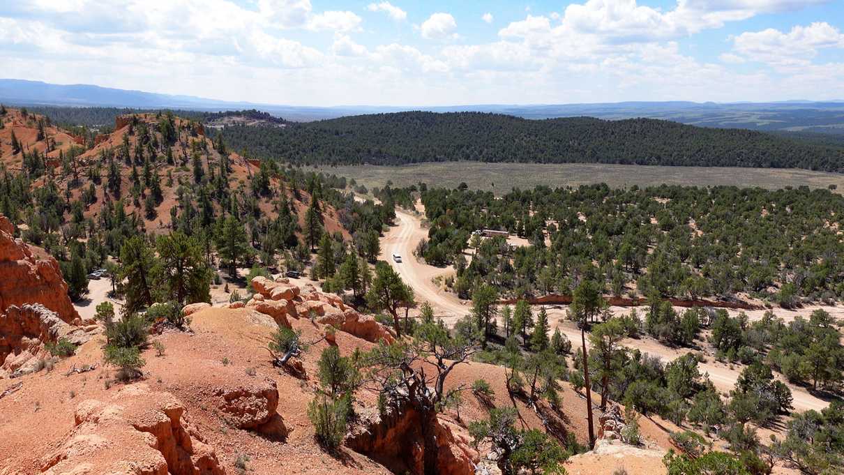 View down from red rocks of dirt road leading to parking lots amid green trees