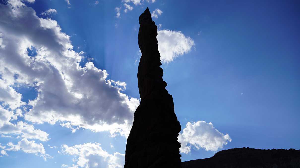 Silhouette of a rock spire with blue sky and clouds and background