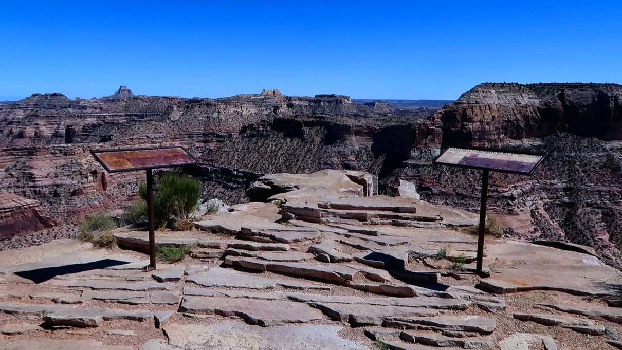 Two signs at the edge of a rock outcropping above canyon