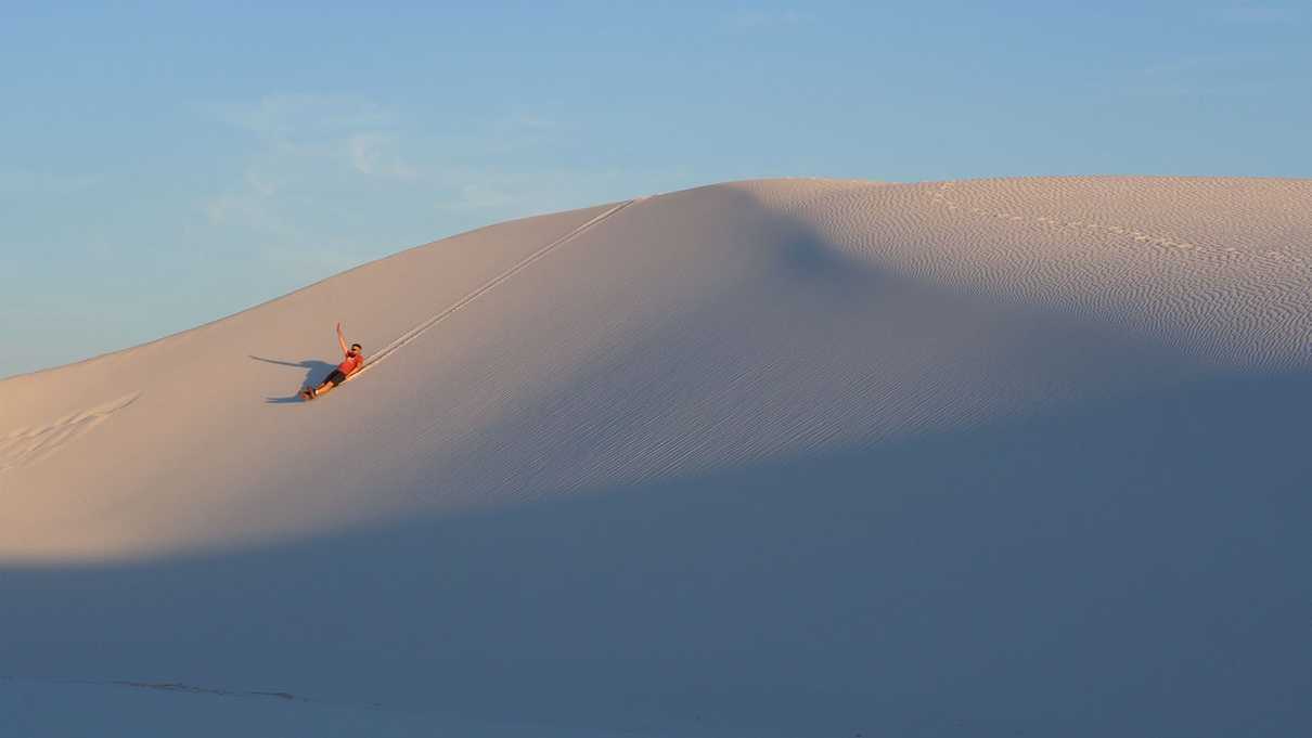 Male figure sliding down a sand dune