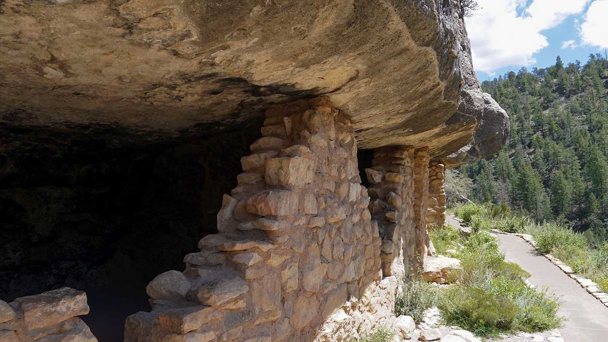 Paved walkway next to remnants of stone wall from cliff dwelling