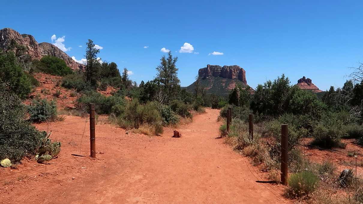 A red dirt path leads to large rock formations in the background