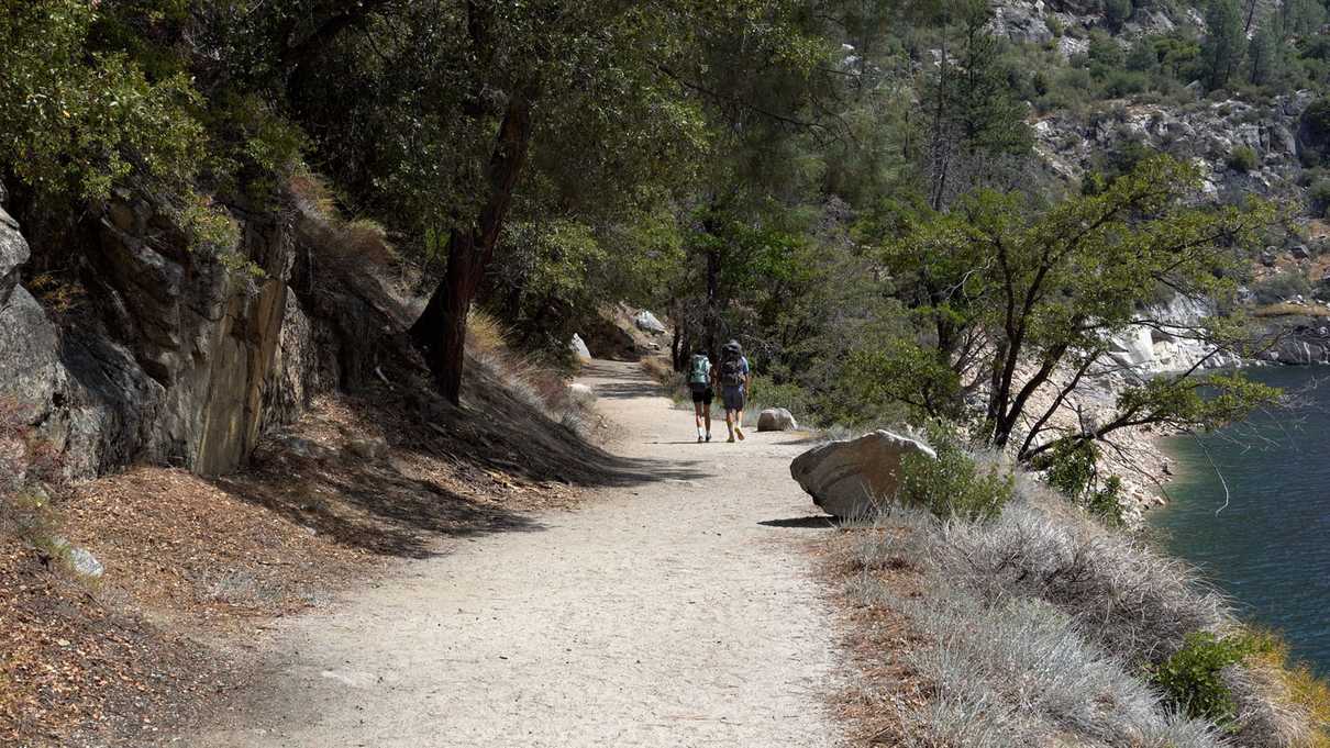 Two hikers walk down dirt trail next to body of water