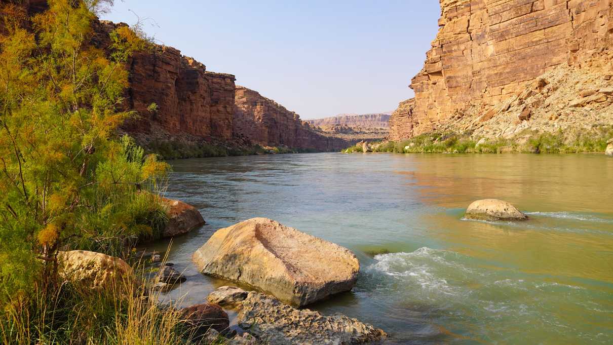 Two large rocks in a green-tinged river flowing through deep red canyon walls