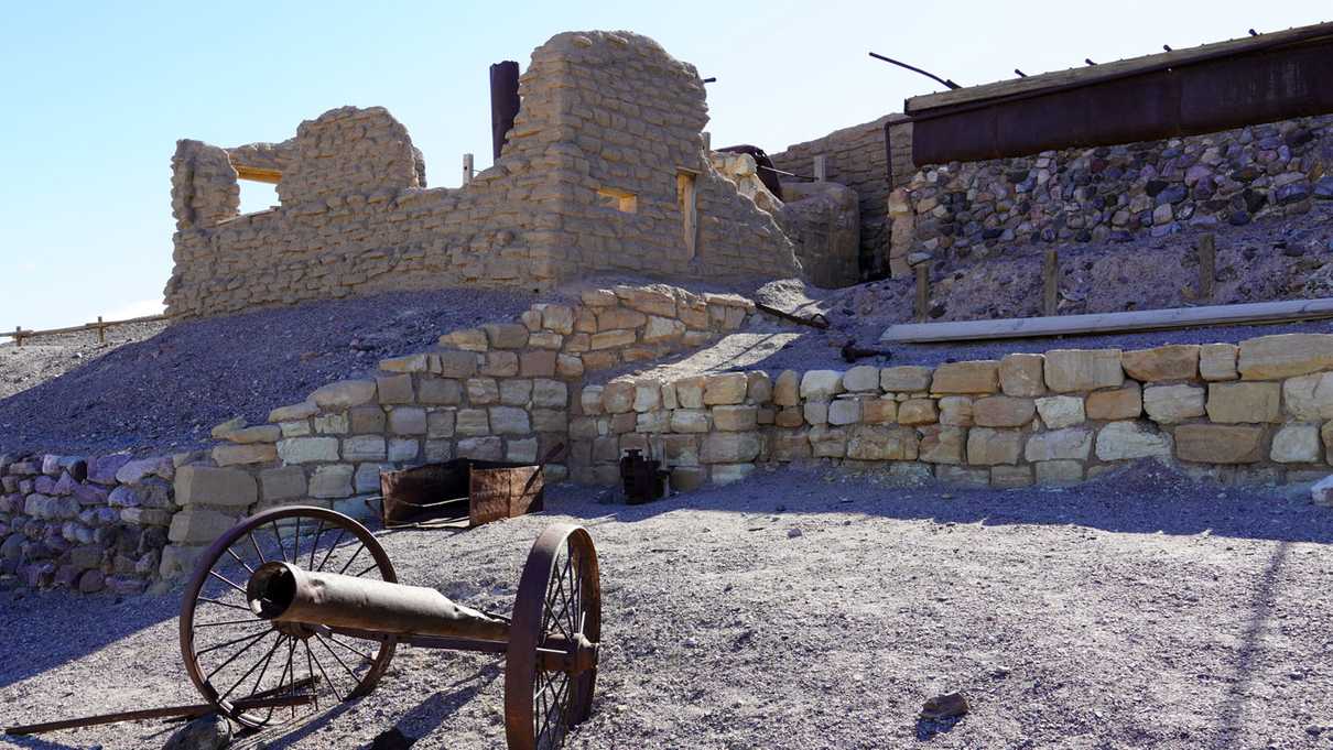Metal scrap remains with ruins of adobe building in background