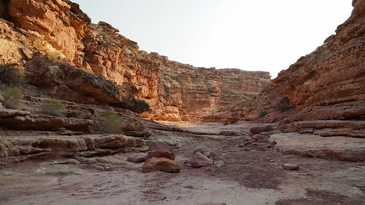 Rocks and debris lie in a dry river bed between red canyon walls