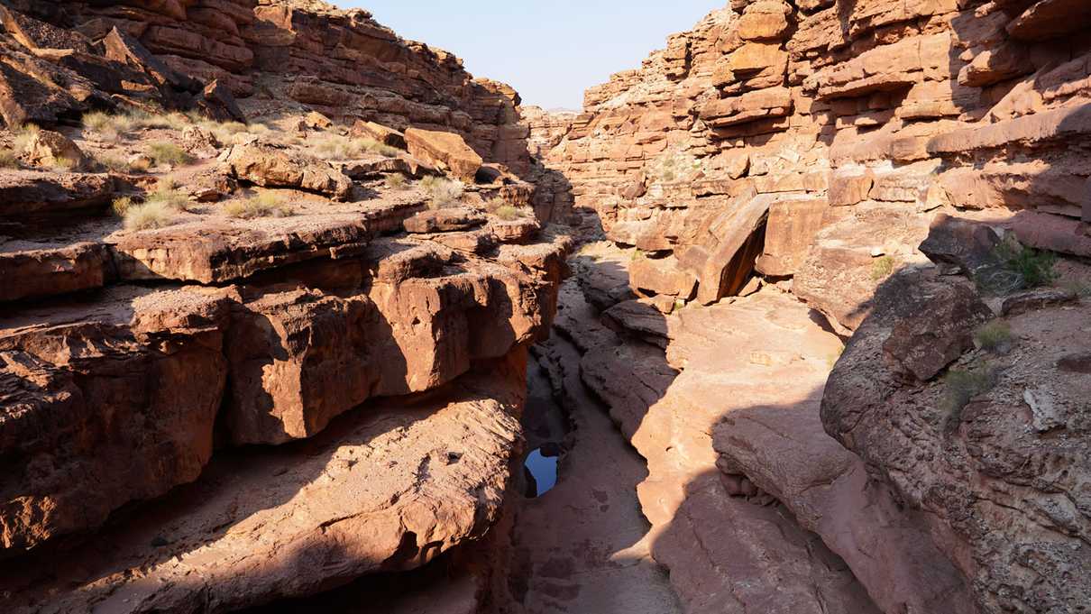 Puddles of water sit at the bottom of multiple levels of red rock canyon walls