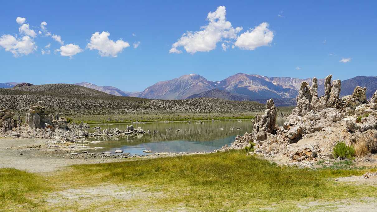 Tufa in foreground by lakeside with mountains and blue sky