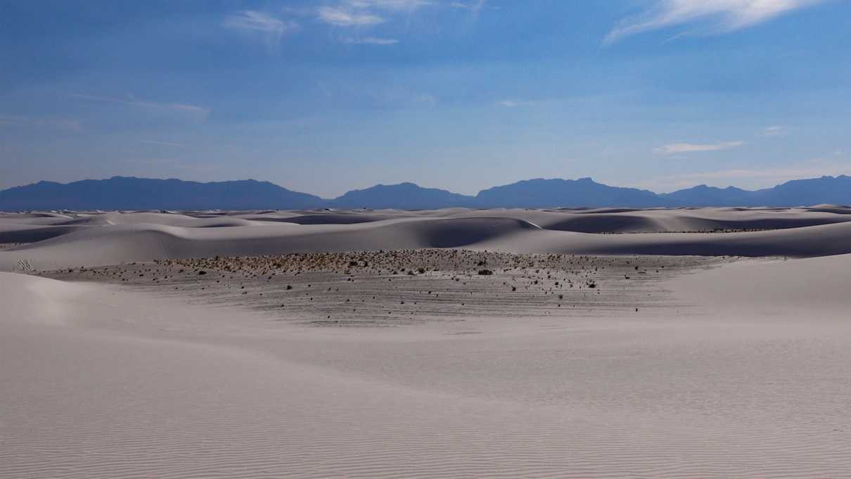Layers of rolling white sand dunes with mountains in background