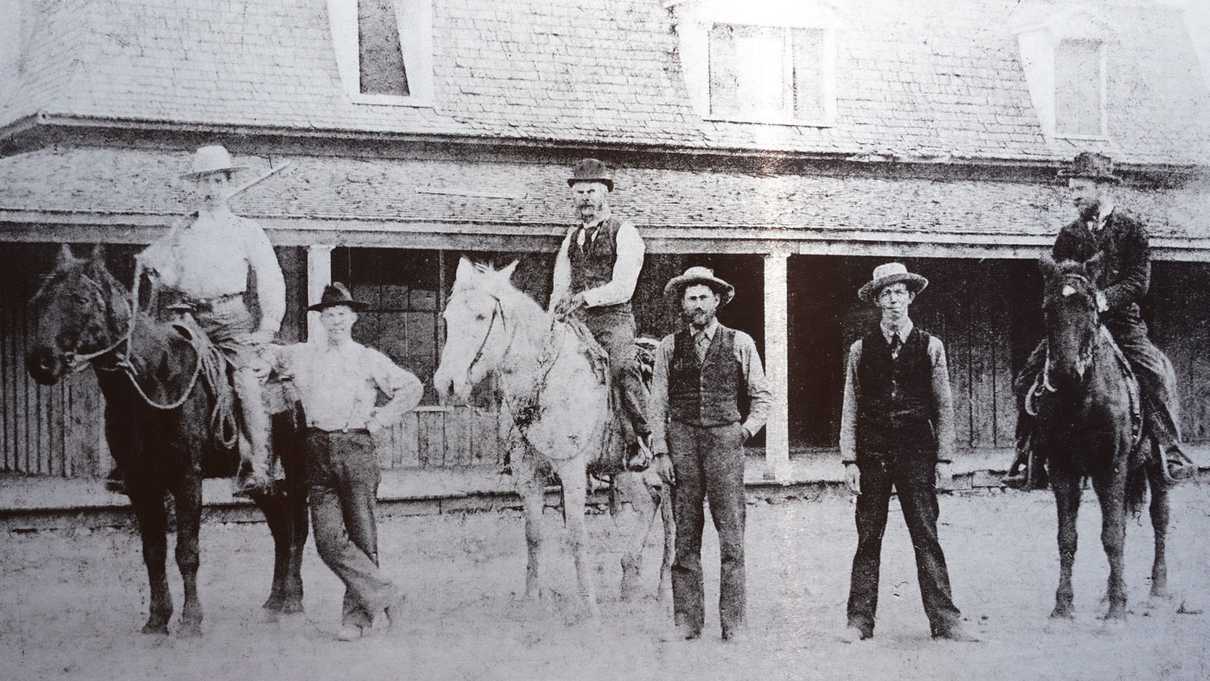 Black and white photo of people and horses in front of house