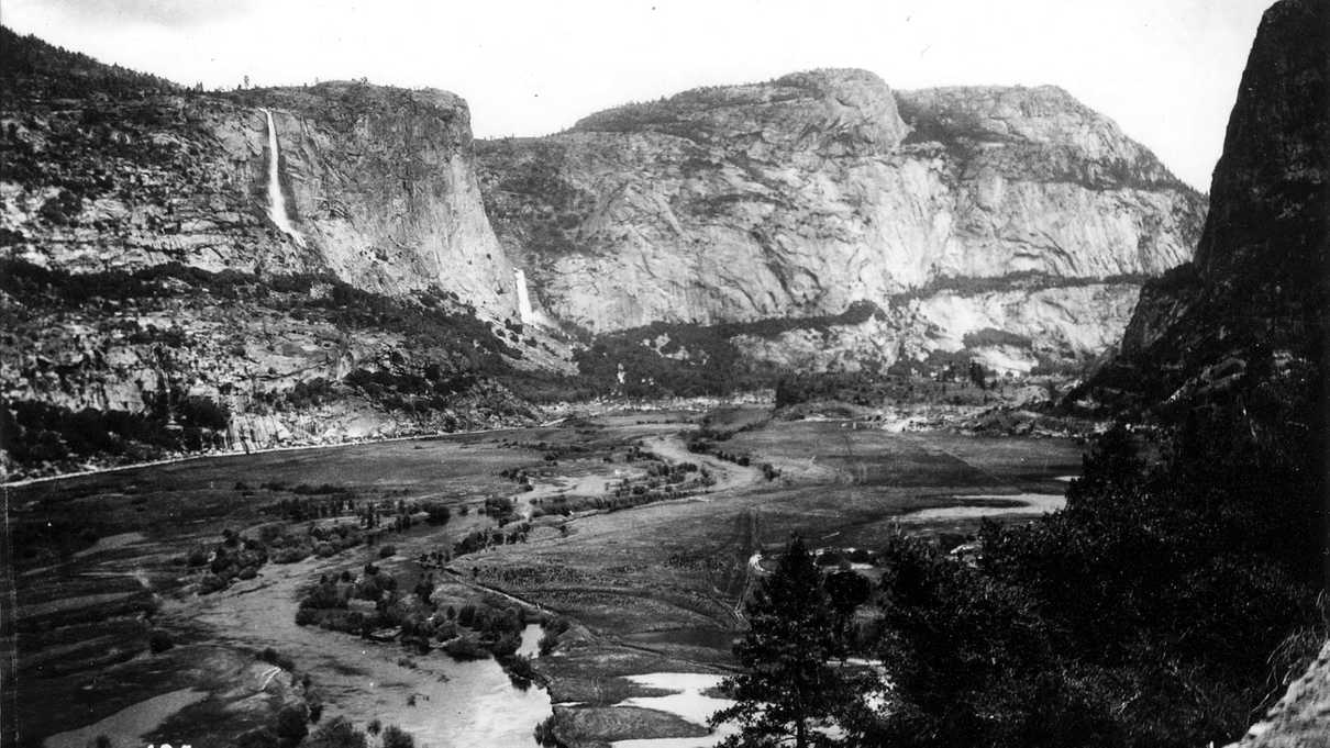 Black and white photo of grey rock with waterfalls and water running through valley