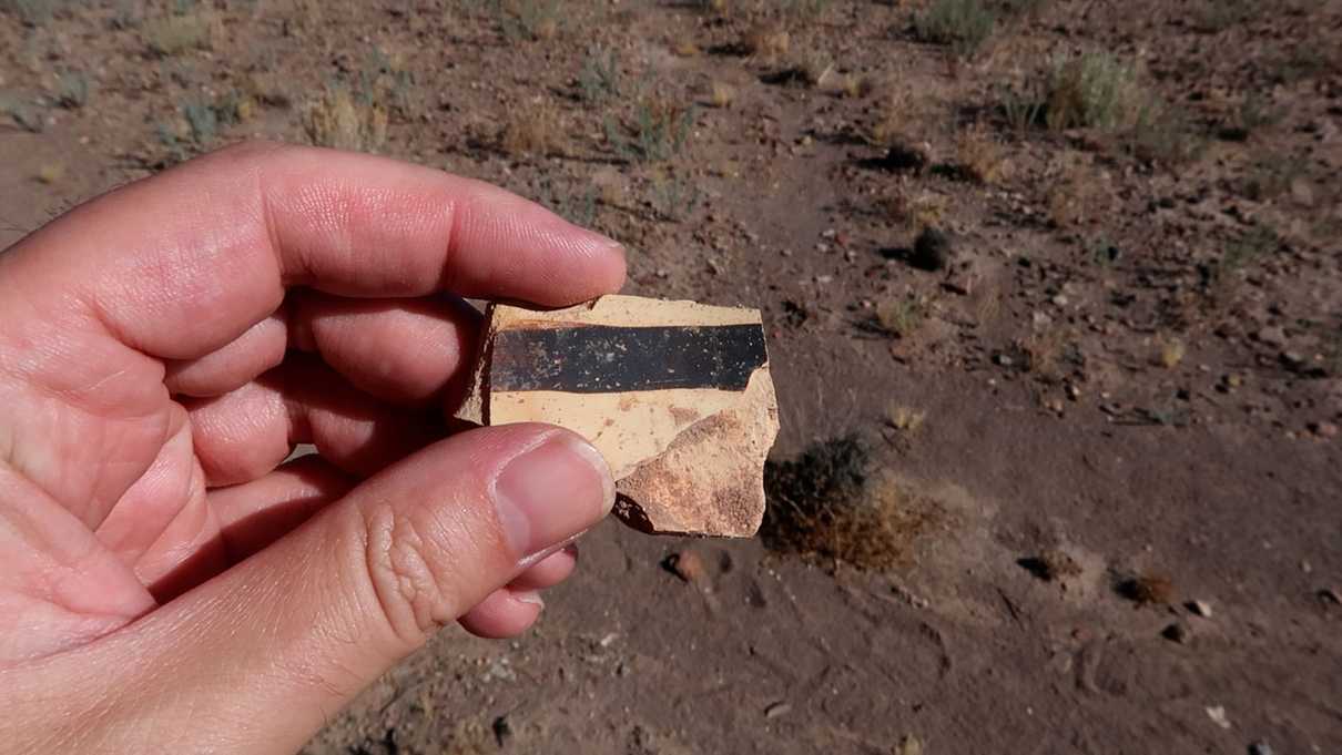 Closeup of hand holding painted pottery fragment