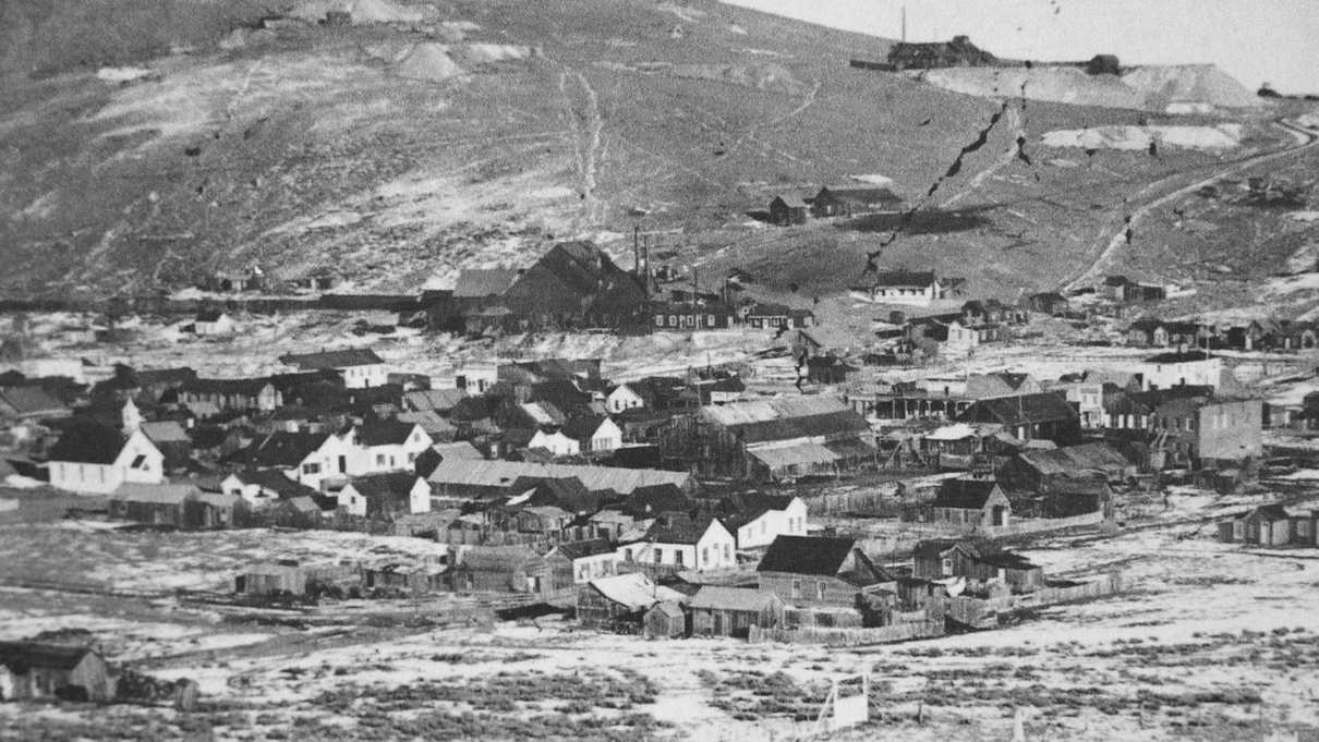 Old black and white photo of mining town consisting of wooden buildings on hillside