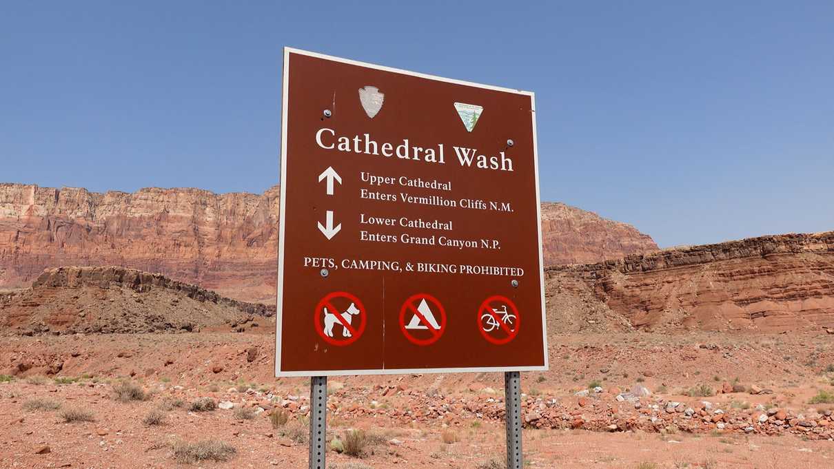 Sign for Cathedral Wash trails and red striped canyon walls in the background