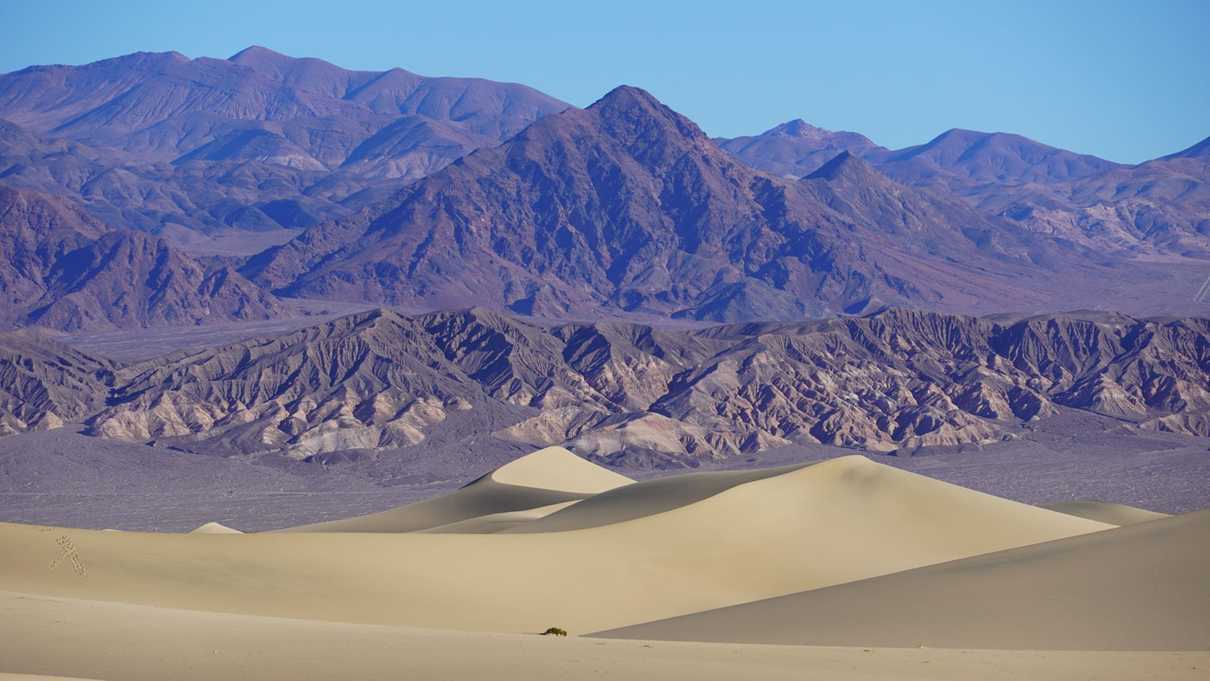 Layers of sand dunes against background of red toned mountain range