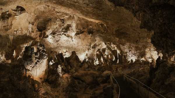 A paved trail winds though an underground cavern filled with stalagmites and stalactites