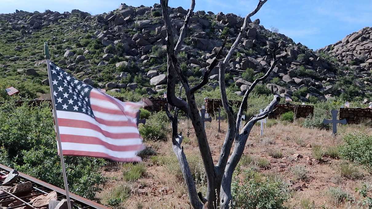 A flag in the wind in front of a charred dead tree at the Granite Mountain Hotshots memorial site