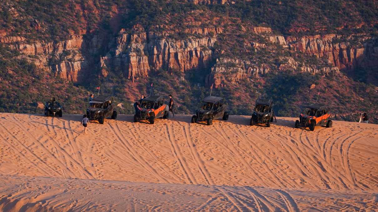 Five off-highway vehicles parked on top of a ridge of a sand dune