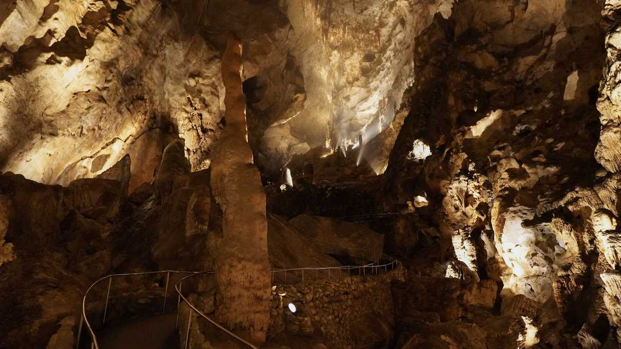 A paved trail winds though an underground cavern filled with stalagmites and stalactites