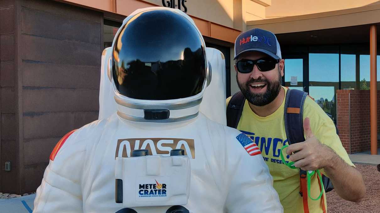 Man giving thumbs up next to astronaut statue