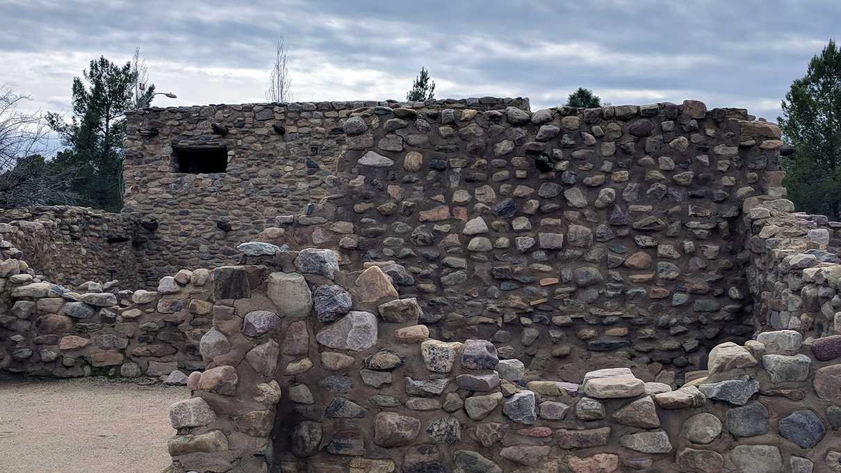 Two story building in background with stone walls of various elevations in foreground