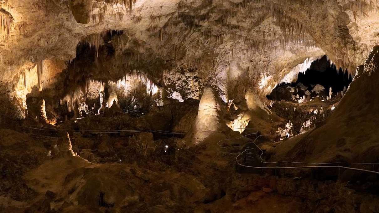 A paved trail winds though an underground cavern filled with stalagmites and stalactites