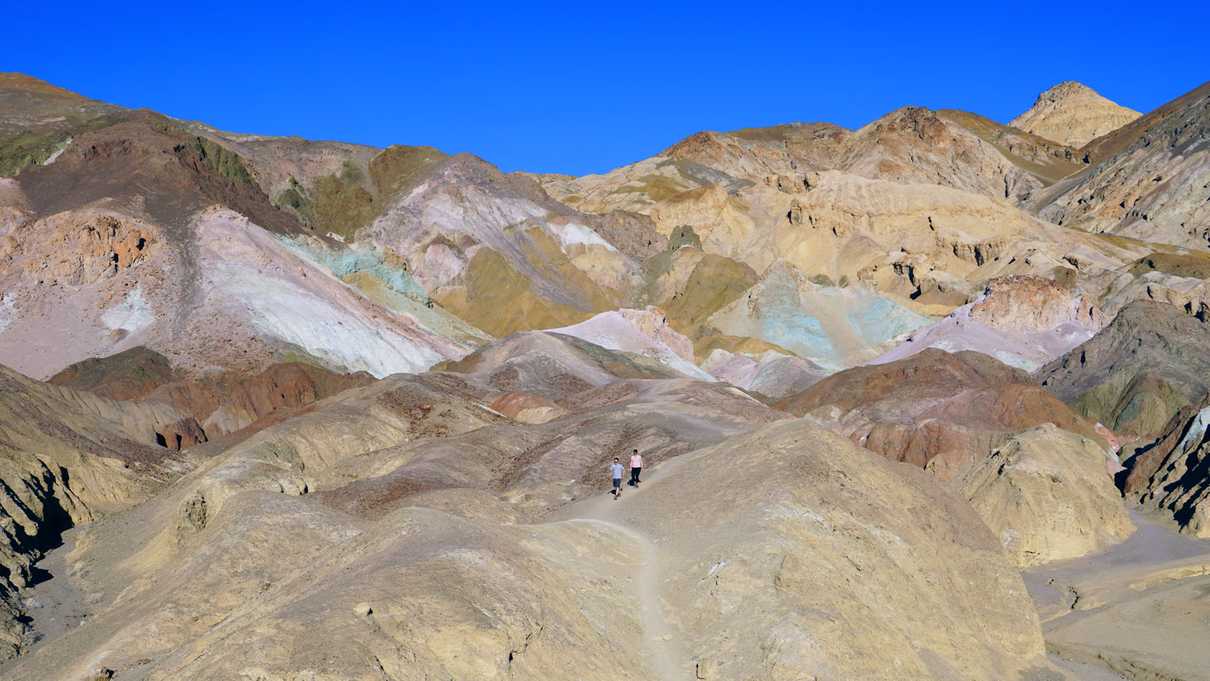 Two people walking with bands of colored hills in background