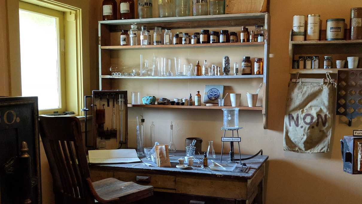 Wooden table and shelves filled with old glass bottles and assaying equipment