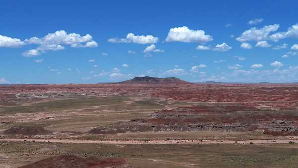 Green valley with red rising hills and mountain peak in distance