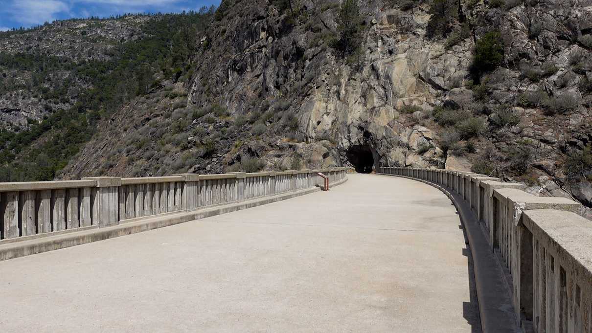 Concrete walkway on top of dam with tunnel in mountain at end