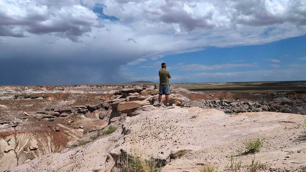 Man stands at edge of overlook with a storm on horizon