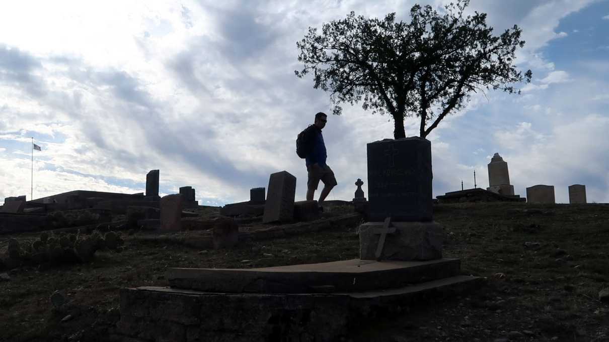 Silhouette of a man walking up a hillside among headstones
