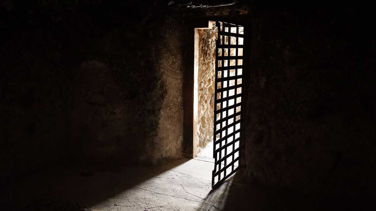 A dark room with light streaming through iron cell door