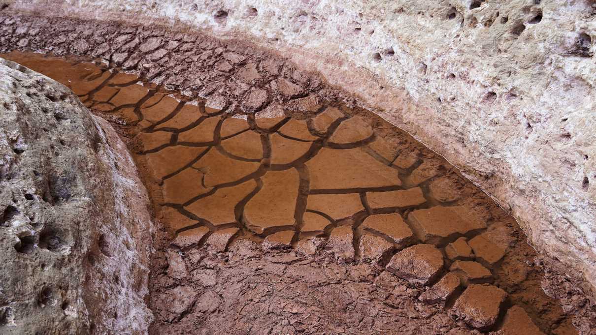 Cracked mud lies underneath standing water at the bottom of canyon floor