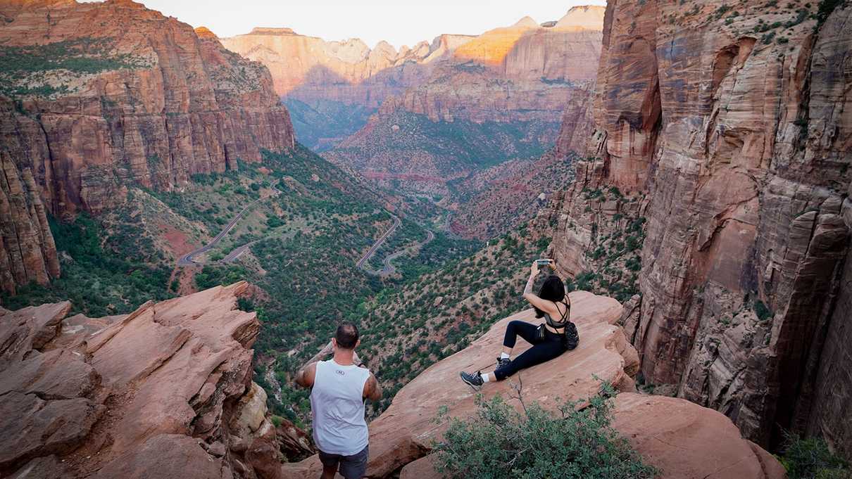 Two figures at the edge of overlook taking photos of sunlit valley below