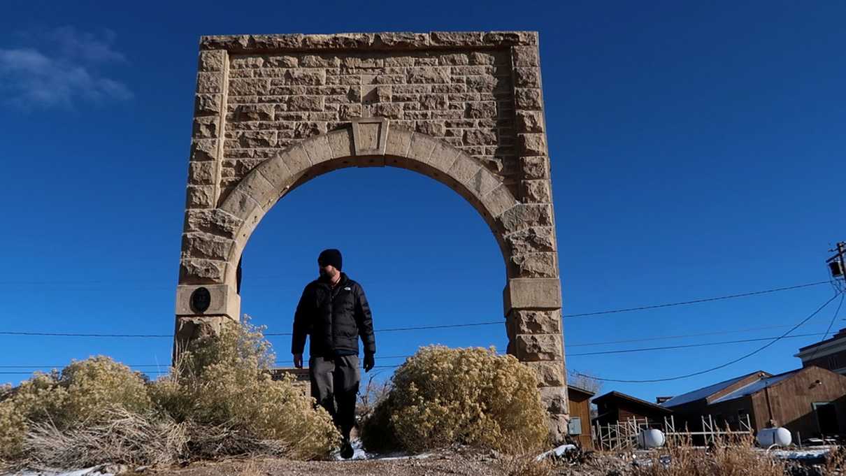 Man standing under stone arch remains of an old saloon